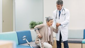 An older woman gets assistance standing from a doctor