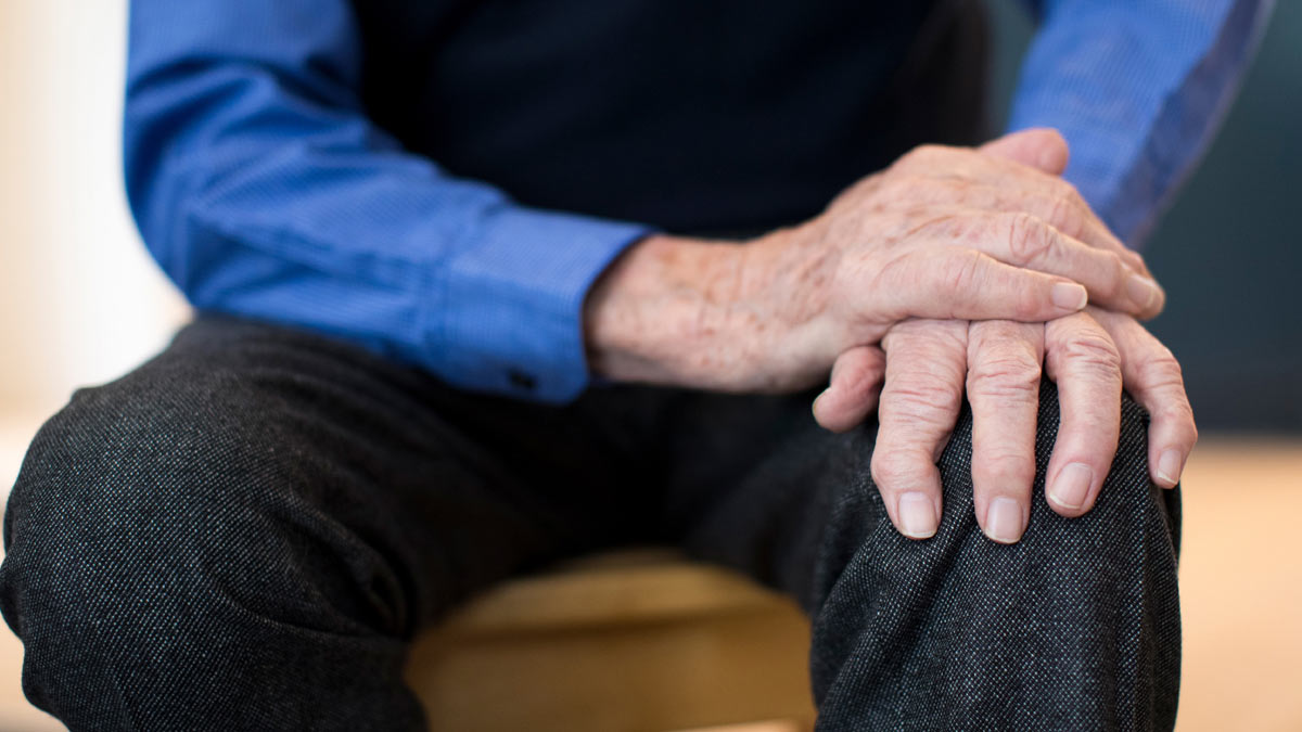 An elderly man with his hands on his knee