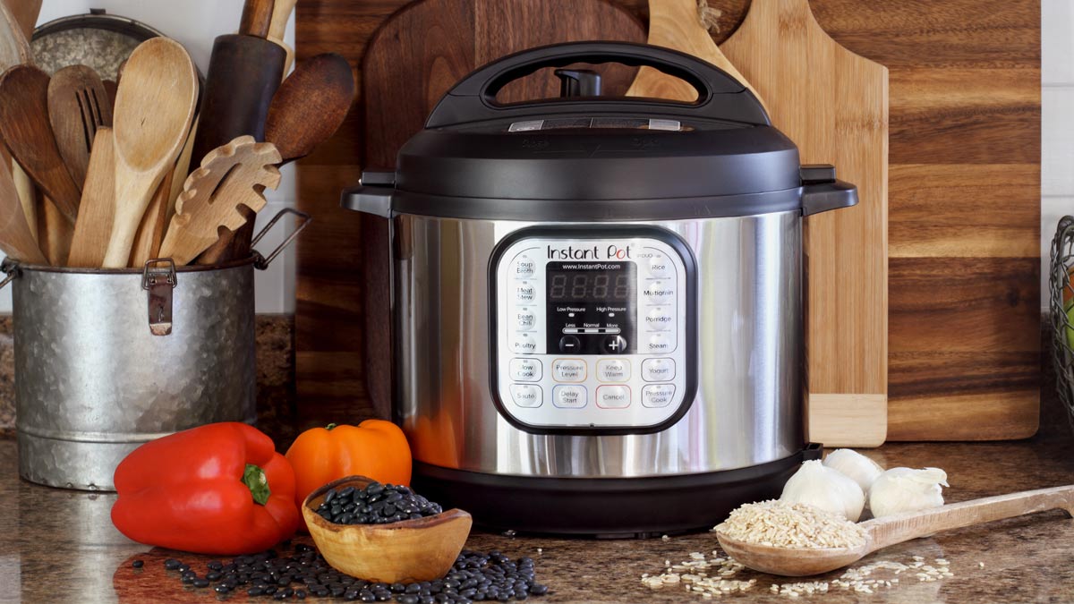 An Instant Pot, wooden utensils, bell peppers, black beans, rice and garlic.