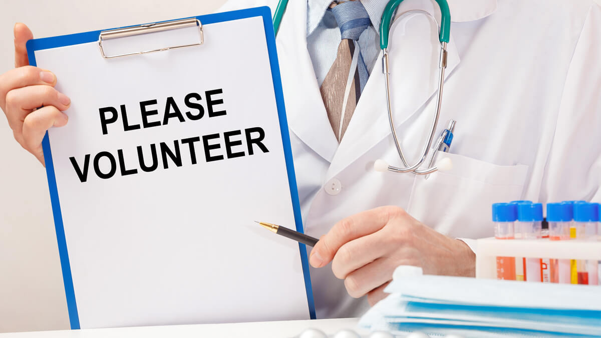 Doctor holding Please Volunteer sign for Clinical Studies