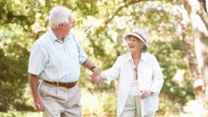 An older man and woman walk outside hand in hand