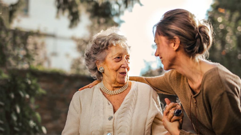 A senior visits with her daughter in a garden outdoors.