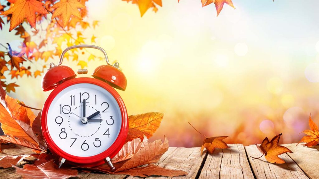 Photo of a clock in front of fall colored leaves